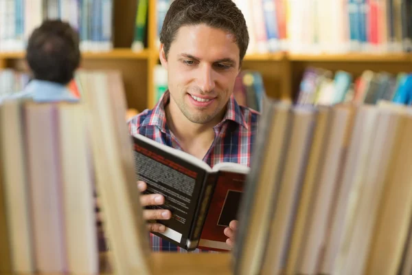 Mature student reading book by shelf in the library — Stock Photo, Image