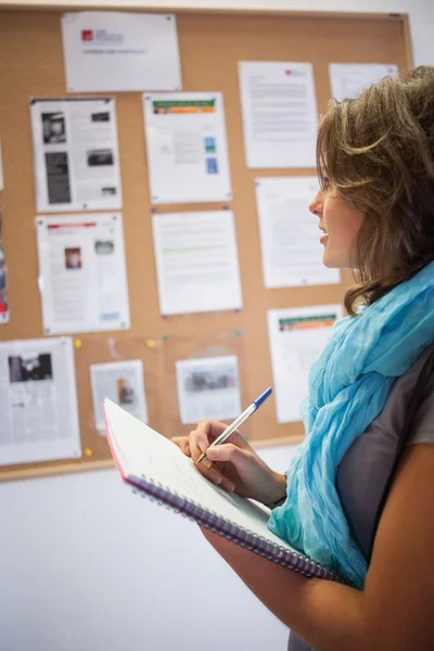 Casual student taking notes in front of notice board — Stock Photo, Image