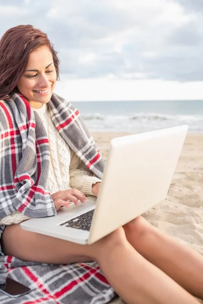 Donna coperta con coperta utilizzando il computer portatile in spiaggia — Foto Stock