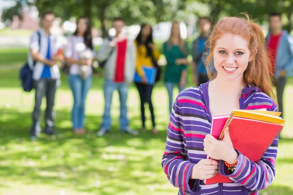 Chica universitaria sosteniendo libros con estudiantes en el parque — Foto de Stock