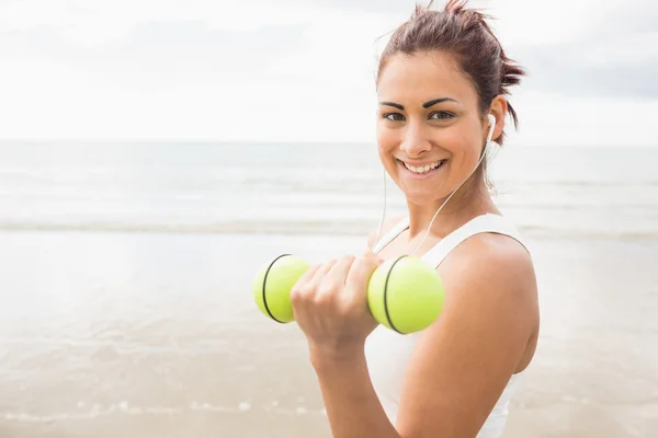 Smiling sporty woman lifting dumbbells on the beach — Stock Photo, Image