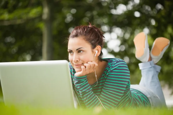 Thoughtful casual student lying on grass using laptop — Stock Photo, Image