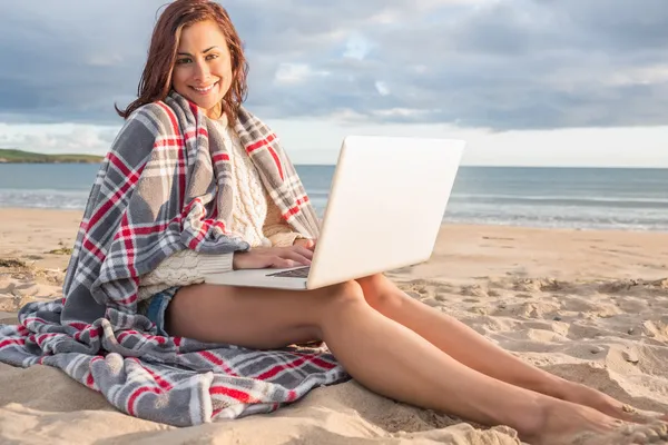 女子盖条毯子，在海滩上使用便携式计算机 — 图库照片