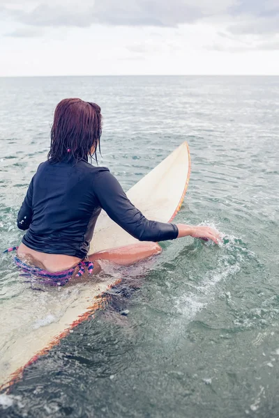 Vista posteriore di una donna seduta sulla tavola da surf in acqua — Foto Stock