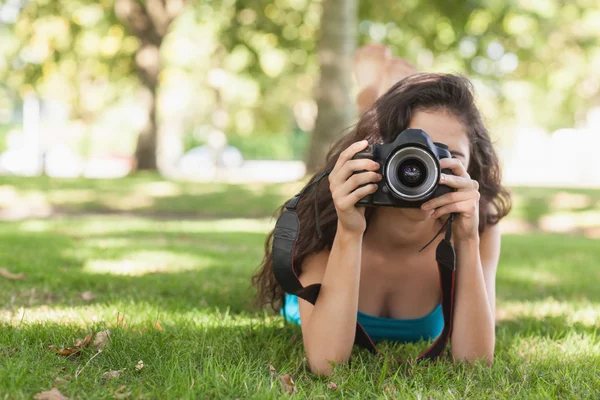 Framifrån av brunett kvinna liggande på en gräsmatta för att ta en bild — Stockfoto