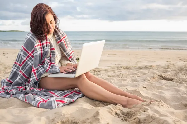 Donna coperta con coperta utilizzando il computer portatile in spiaggia — Foto Stock