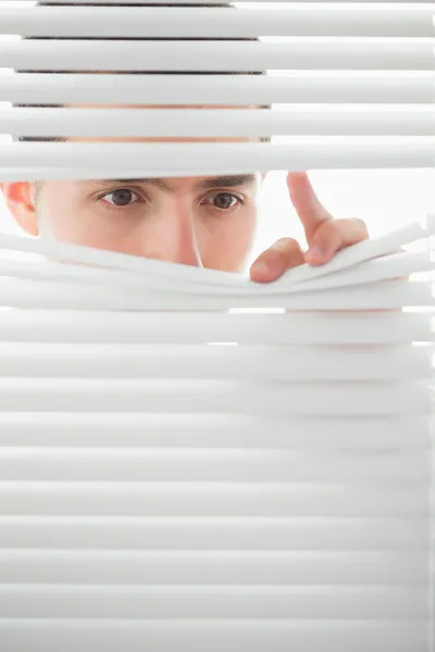 Serious male eyes spying through roller blind — Stock Photo, Image