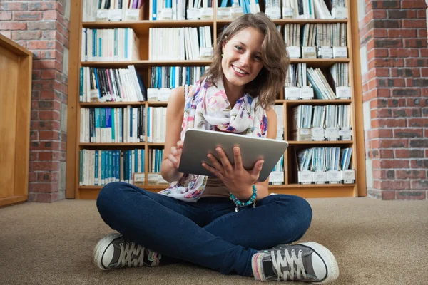 Estudante feliz contra estante com tablet PC na biblioteca fl — Fotografia de Stock