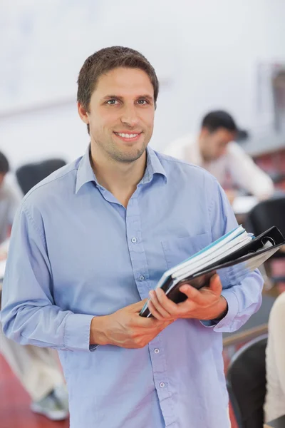 Cute male teacher holding some files while posing in his classro — Stock Photo, Image