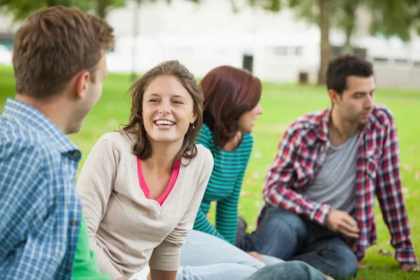 Casual riendo estudiantes sentados en la hierba charlando — Foto de Stock