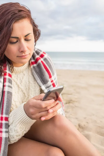 Mujer cubierta con manta usando celular en la playa — Foto de Stock