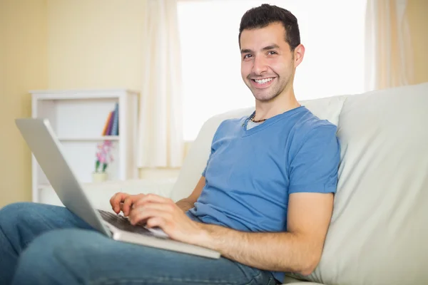 Man sitting on couch using laptop looking at camera — Stock Photo, Image