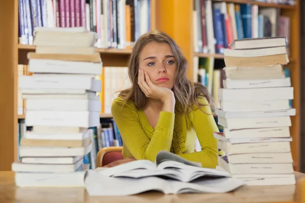 Thoughtful pretty student studying between piles of books — Stock Image Thoughtful pretty student studying between piles of books Royalty Free Stock Images