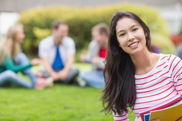 Usměvavý student s rozmazané přátel v parku — Stock fotografie