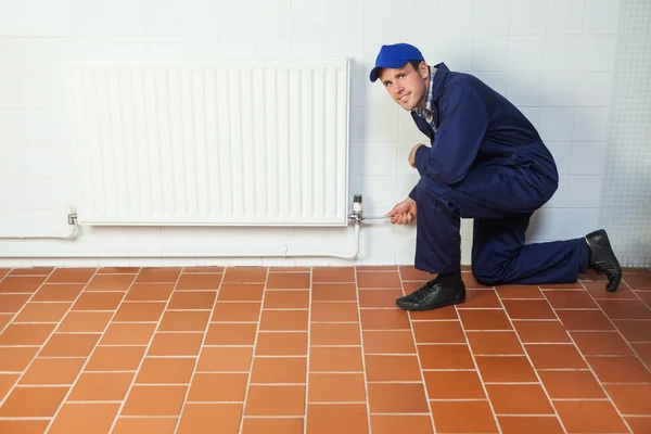 Handyman en traje de caldera azul reparando un radiador sonriendo a cam —  Fotos de Stock