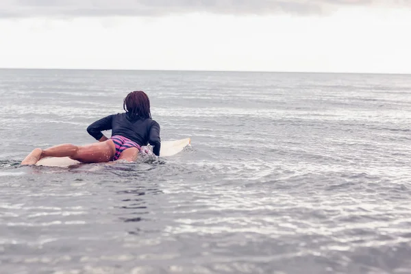 Vista trasera de una mujer sobre tabla de surf en agua —  Fotos de Stock