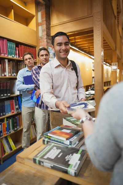 Homem atraente entregando um livro para a bibliotecária feminina — Fotografia de Stock