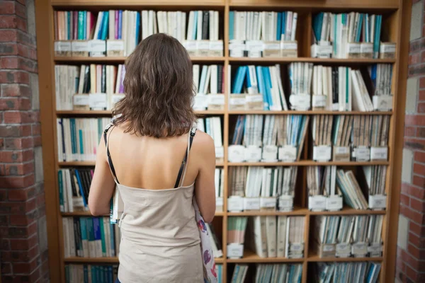 Rear view of a student at bookshelf in the library — Stock Photo, Image