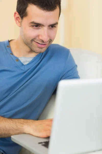 Uomo contenuto casuale seduto sul divano utilizzando il computer portatile — Foto Stock