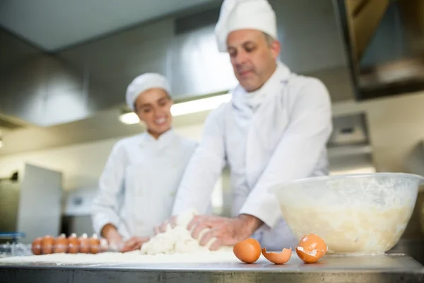 Шеф-повар показывает улыбающемуся стажеру, как готовить тесто — стоковое фото