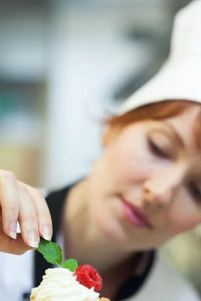 Jefe de cocina concentrado poniendo hoja de menta en el pequeño pastel — Foto de Stock