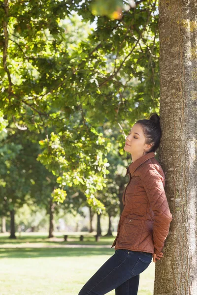 Attraktive Frau lehnt mit geschlossenen Augen an einem Baum — Stockfoto