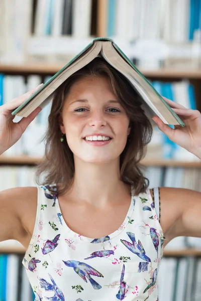 Estudante feminina segurando livro sobre sua cabeça na biblioteca — Fotografia de Stock