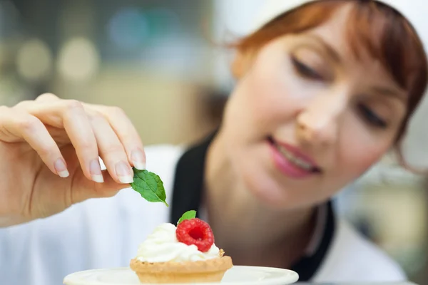 Happy head chef putting mint leaf on little cake — Stock Photo, Image