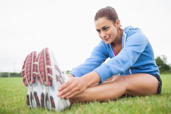 Sportif kadın çimenlerin üzerinde otururken bacaklarını germe — Stok fotoğraf