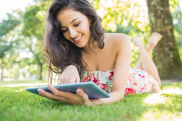 Stylish cheerful brunette lying on a lawn using tablet — Stock Photo, Image