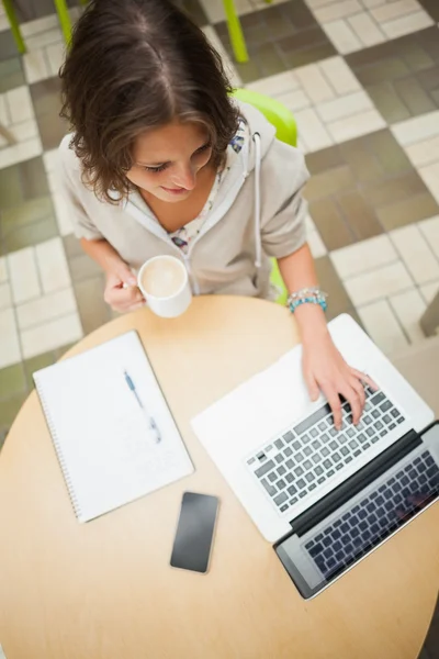 Student trinkt Kaffee, während er Laptop am Cafeteria-Tisch benutzt — Stockfoto