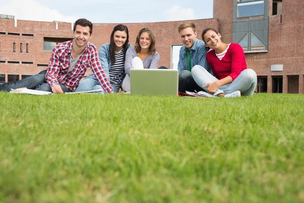 Estudantes com laptop no gramado contra prédio universitário — Fotografia de Stock