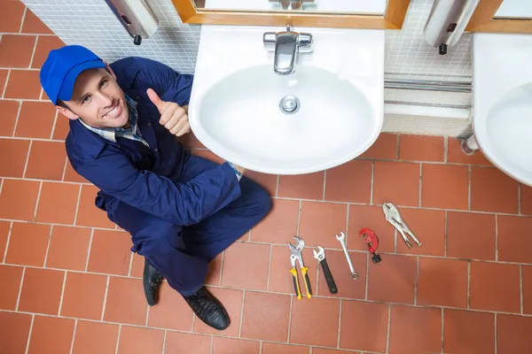 Fröhlicher Klempner repariert Waschbecken und zeigt Daumen hoch — Stockfoto