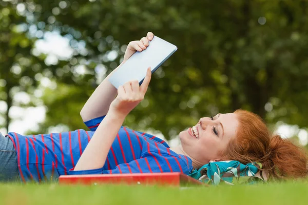Nádherná usměvavá student ležící na trávě pomocí tabletu — Stock fotografie