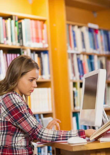 Досить зосереджений студент читає книгу за допомогою комп'ютера — стокове фото