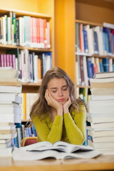 Trött student mellan högar av böcker med slutna ögon — Stockfoto