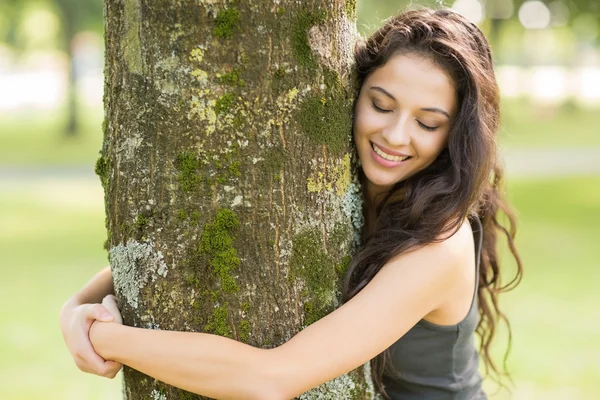 Lässige, fröhliche Brünette, die mit geschlossenen Augen einen Baum umarmt — Stockfoto