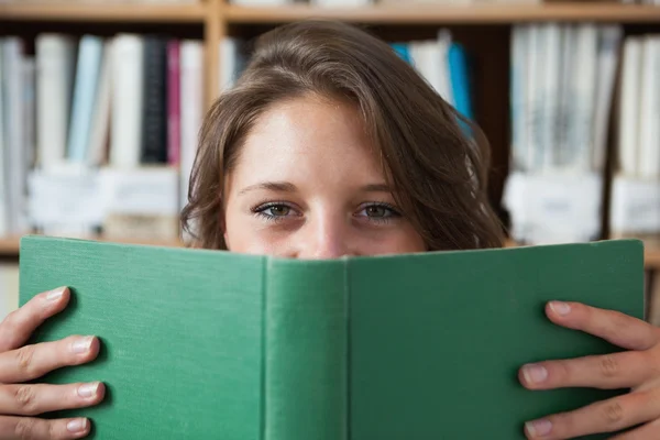 Vrouwelijke student boek voor haar gezicht bedrijf in bibliotheek — Stockfoto