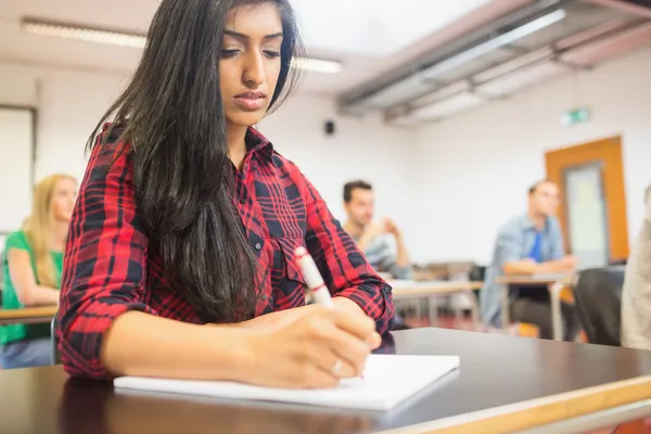 Vrouwelijke student met anderen schrijven nota's in de klas — Stockfoto