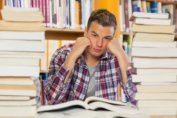 Estudante bonito irritado estudando entre pilhas de livros — Fotografia de Stock