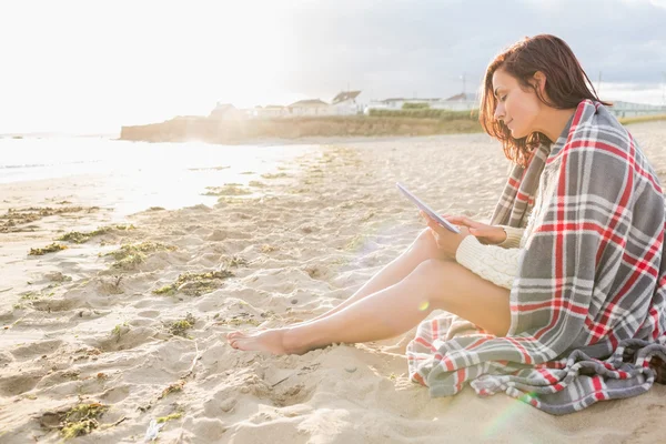 Woman covered with blanket using tablet PC at beach — Stock Photo, Image