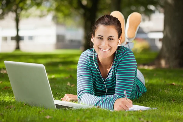 Glücklicher Gelegenheitsstudent, der im Gras liegt und Notizen macht — Stockfoto