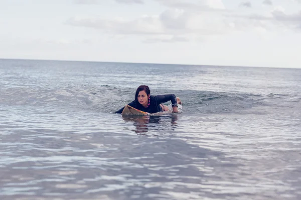 Mujer joven nadando sobre tabla de surf en el agua —  Fotos de Stock
