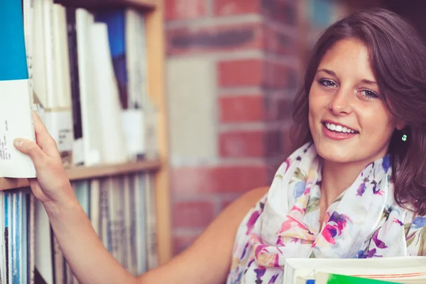 Kvinnlig student att välja bok från hyllan i biblioteket — Stockfoto