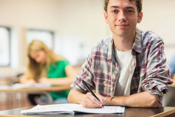 Lächelnder Schüler mit anderen, die im Klassenzimmer Notizen schreiben — Stockfoto