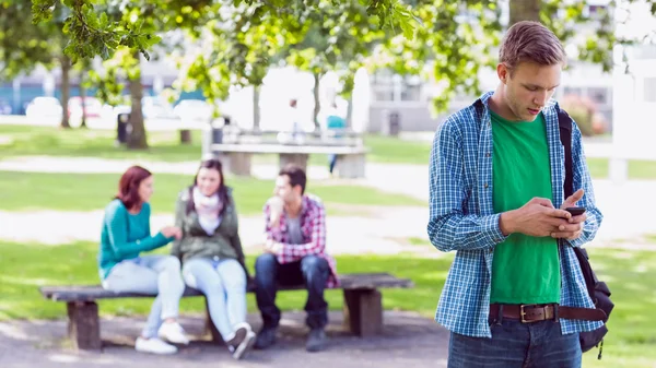 College boy messaggistica di testo con gli studenti offuscati nel parco — Foto Stock