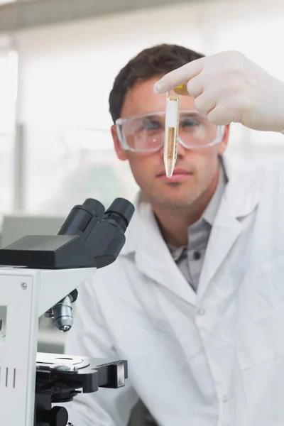 Scientific researcher looking at test tube while using microscop — Stock Photo, Image