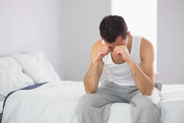 Sleepy casual man sitting on bed rubbing his eyes — Stock Photo, Image