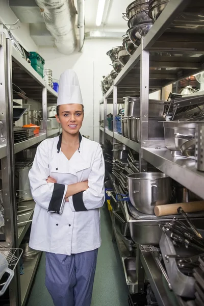 Young smiling chef standing arms crossed between shelves — Stock Photo, Image