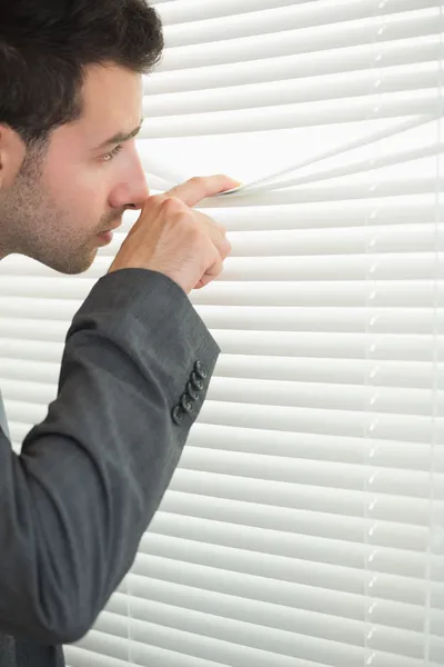 Gutaussehender seriöser Geschäftsmann spioniert durch Rollladen — Stockfoto